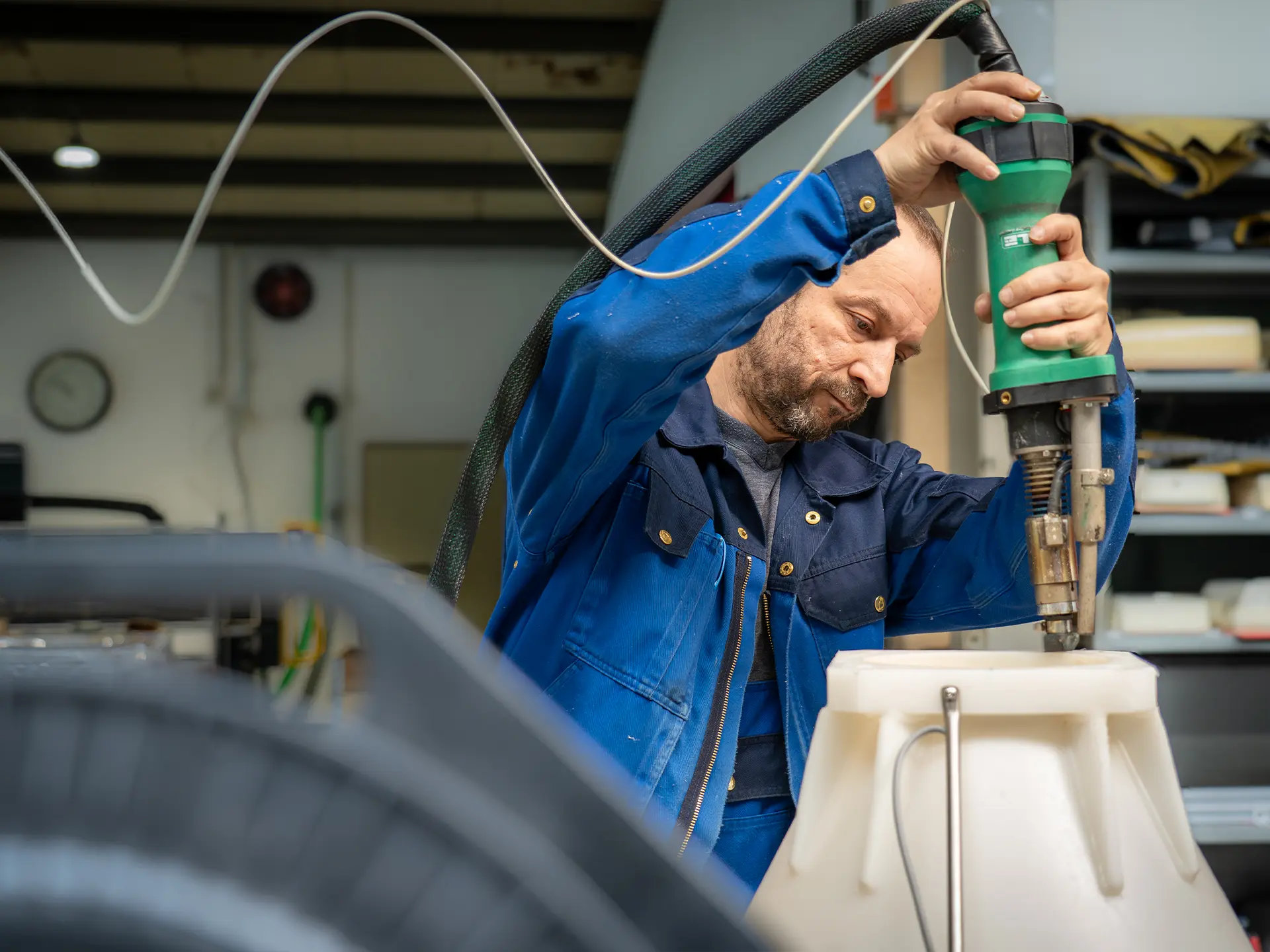 Arbeiter in blauer Jacke bedient ein handgeführtes Elektrowerkzeug an einem weißen Kunststoffbauteil