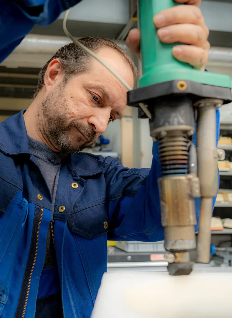 Nahaufnahme eines Handwerkers in blauer Arbeitskleidung, konzentriert beim Bedienen eines grünen elektrischen Werkzeugs an einem Werkstück