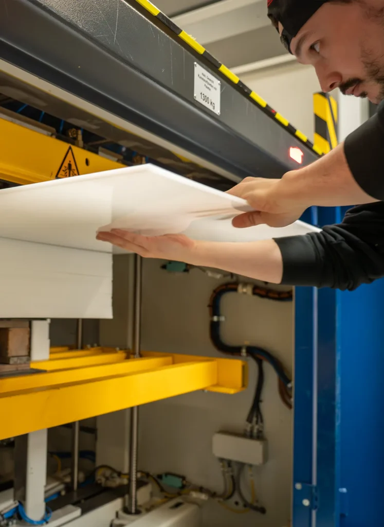 Mitarbeiter schiebt eine weiße Platte in eine industrielle Presse mit gelben Trägern