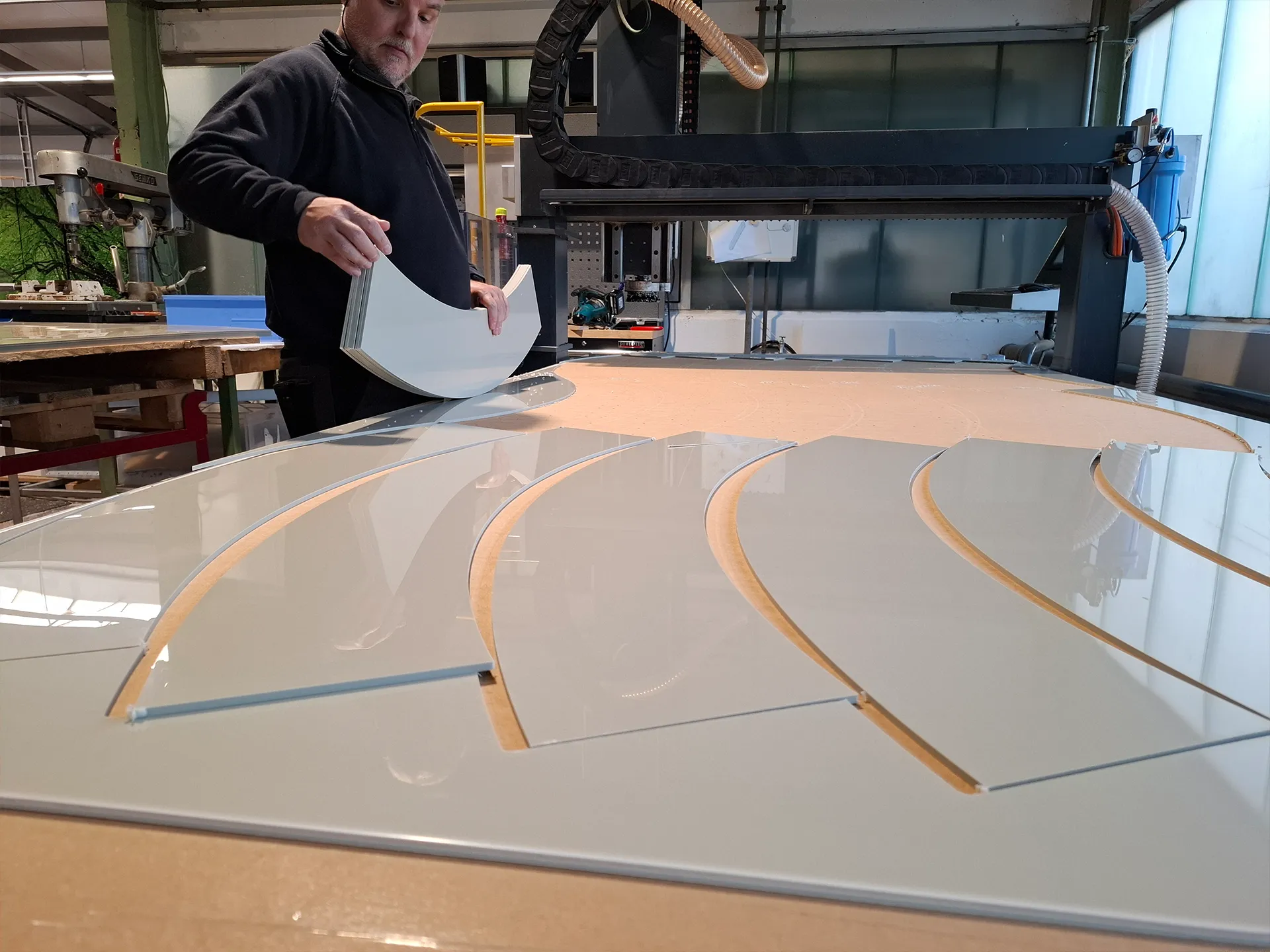 Person in einer Werkstatt hebt gebogene, frisch ausgeschnittene Kunststoffplatten von einer CNC-Maschine